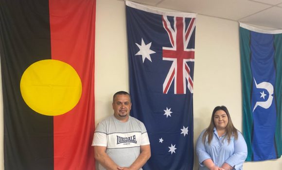 Man and woman posing for photo in front of aboriginal and Australian flags