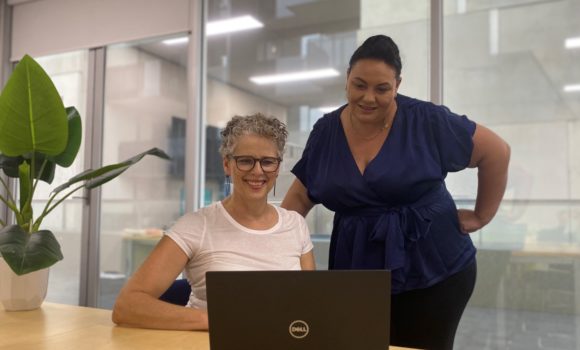 Two women standing in front of laptop talking